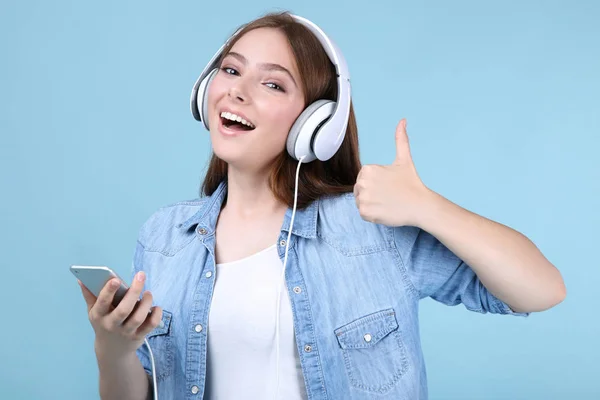 Молода жінка з навушниками та мобільним телефоном на синьому фоні — стокове фото
