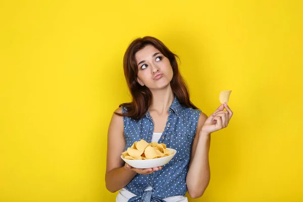 Giovane donna con patatine in piatto su sfondo giallo — Foto Stock