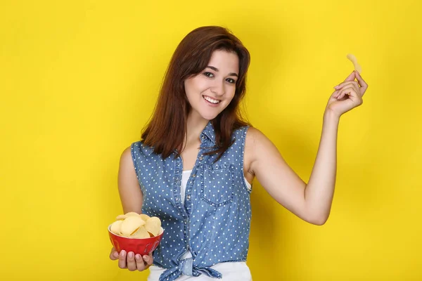 Młoda kobieta z chipami ziemniaczanym w misce na żółtym tle — Zdjęcie stockowe