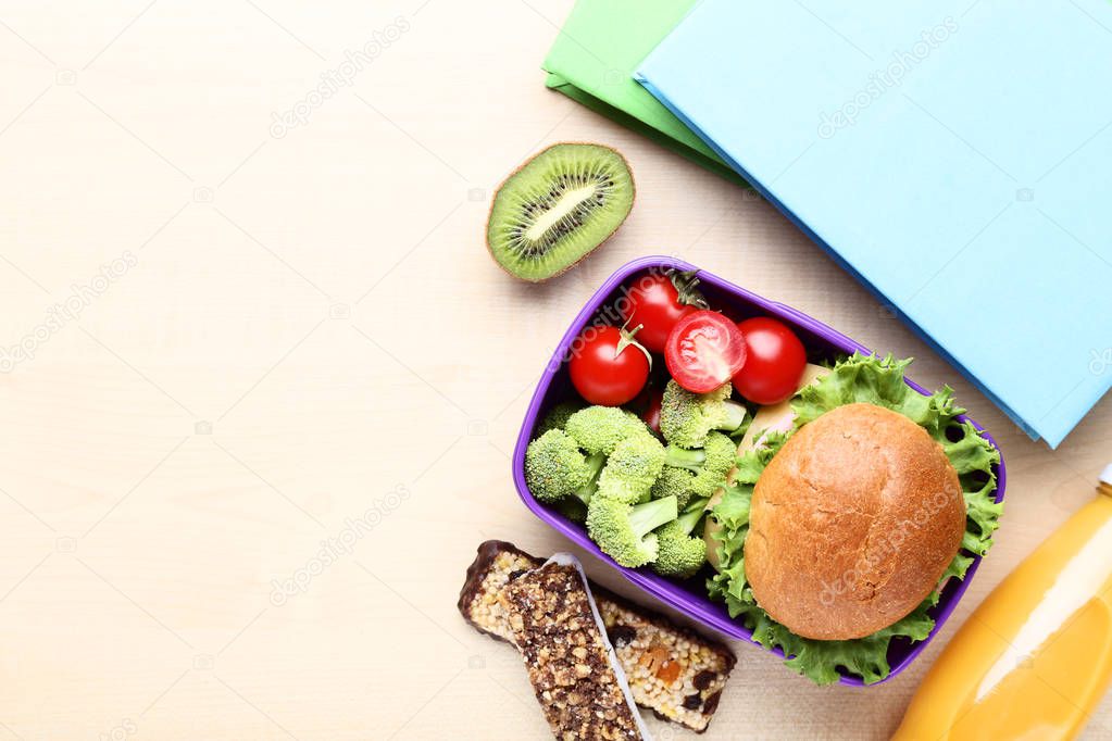 School lunch box with sandwich and books on wooden table
