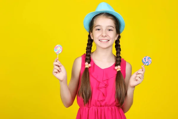 Menina bonita com pirulitos doces no fundo amarelo — Fotografia de Stock