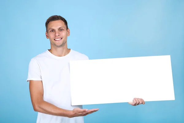 Junger Mann mit leerem Brett auf blauem Hintergrund — Stockfoto