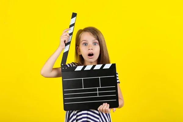 Little girl with clapper board on yellow background — Stock Photo, Image