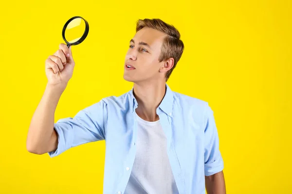 Young man with magnifying glass on yellow background — Stock Photo, Image