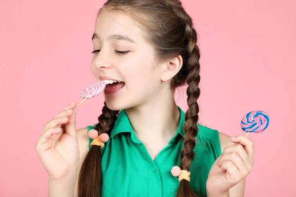 Hermosa chica joven comiendo piruletas dulces sobre fondo rosa —  Fotos de Stock