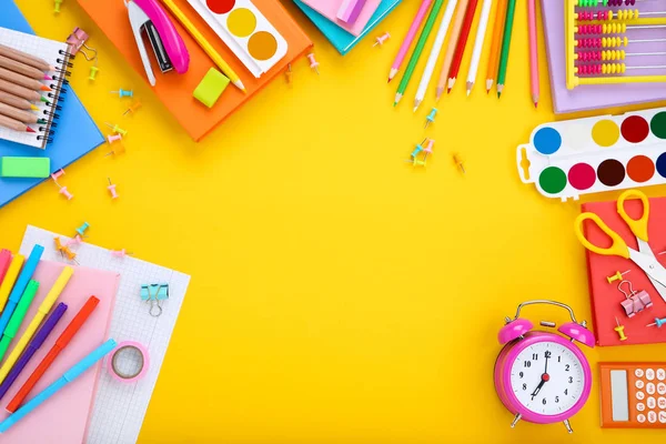 Diversi materiali scolastici con sveglia su sfondo giallo — Foto Stock