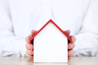 Ahşap ev modelini tutan kadın eller.