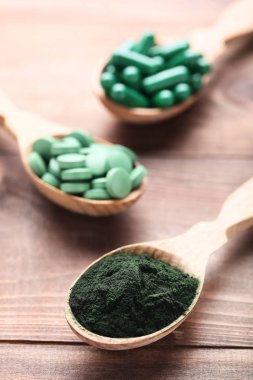 Spirulina tozu ve kaşık kahverengi ahşap masa üzerinde tablet