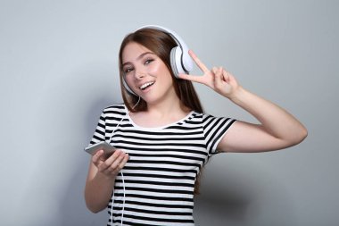 Gri arka planda kulaklık ve cep telefonu ile genç kadın