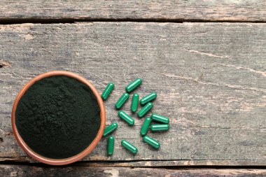 Gri ahşap masa üzerinde Spirulina tozu ve kapsüller