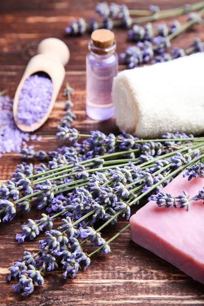 Lavendelblüten mit Öl in der Flasche, Salz und Seife auf braunem Holz — Stockfoto