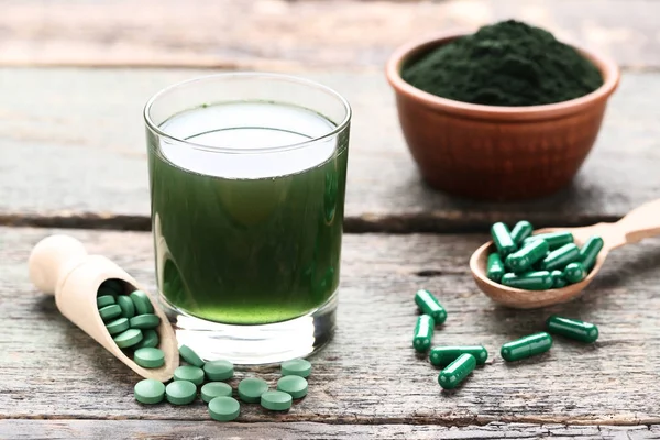 Spirulina drink and pills with powder in bowl on grey wooden tab