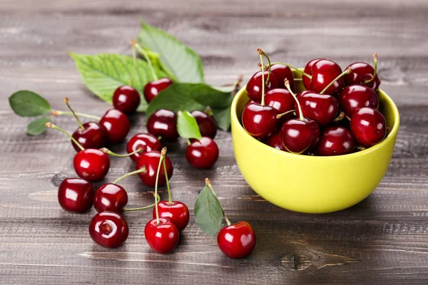 Cerises douces dans un bol avec des feuilles vertes sur une table en bois — Photo