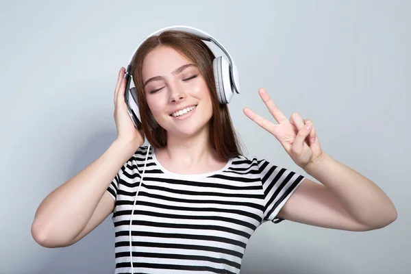 Młoda piękna kobieta z słuchawkami na szarym tle — Zdjęcie stockowe
