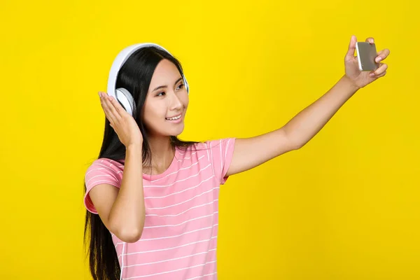 Mujer joven con auriculares haciendo selfie en el teléfono inteligente en yello — Foto de Stock