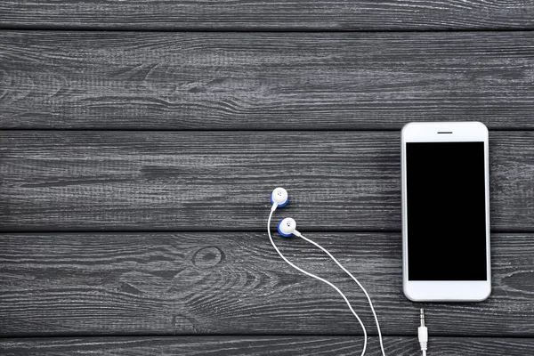 Smartphone with earphones on black wooden table — Stock Photo, Image