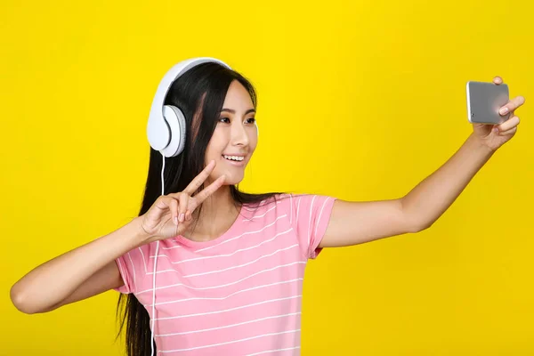 Mujer joven con auriculares haciendo selfie en el teléfono inteligente en yello — Foto de Stock