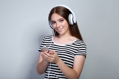 Gri arka planda kulaklık ve cep telefonu ile genç kadın