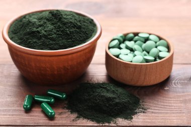 Spirulina tozu ve tabletler kahverengi ahşap masa üzerinde kaselerde