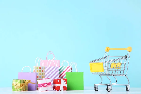 Small cart with gift boxes and shopping bags on blue background — Stock Photo, Image