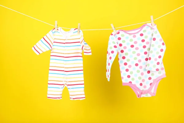 Ropa de bebé colgada sobre fondo amarillo —  Fotos de Stock