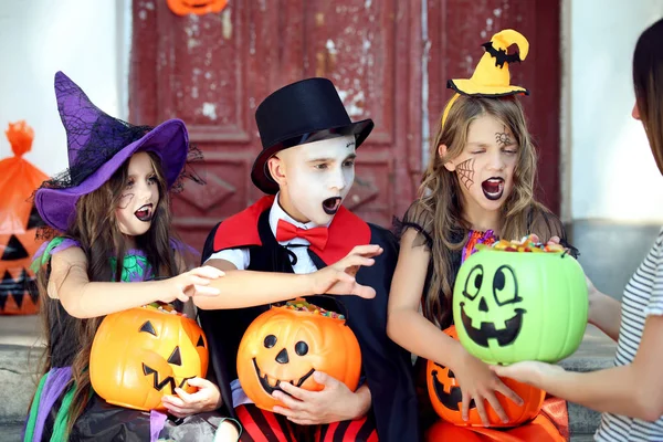 Twee jonge meisjes en jongen in Halloween kostuums zittend op veranda w — Stockfoto