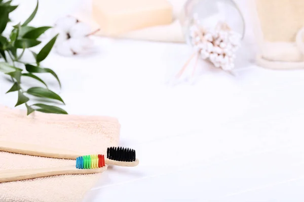 Bamboo toothbrushes with towels, cotton sticks and green leafs on white wooden table — Stock Photo, Image