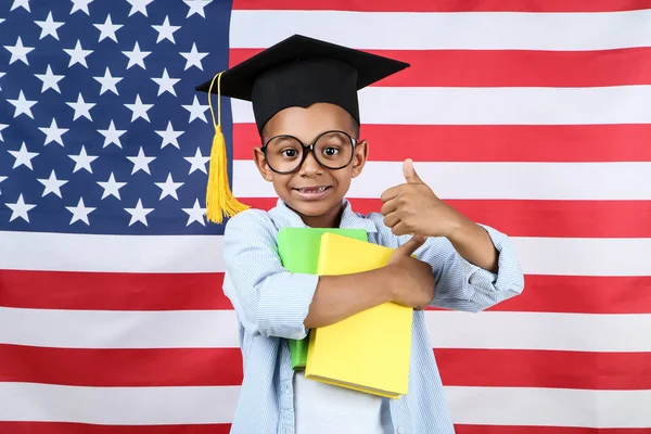 Lindo chico en gorra de graduación con libros sobre fondos de bandera americana — Foto de Stock