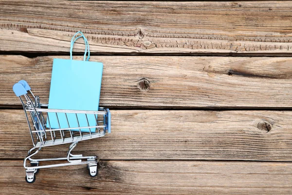 Small metal cart with shopping bags on brown wooden table — Stock Photo, Image