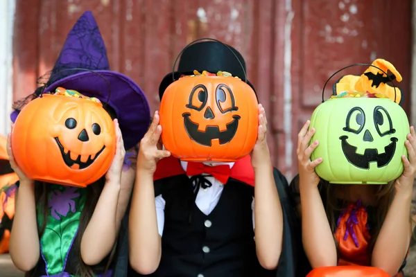Две девочки и мальчик в костюмах на Хэллоуин сидят на крыльце — стоковое фото