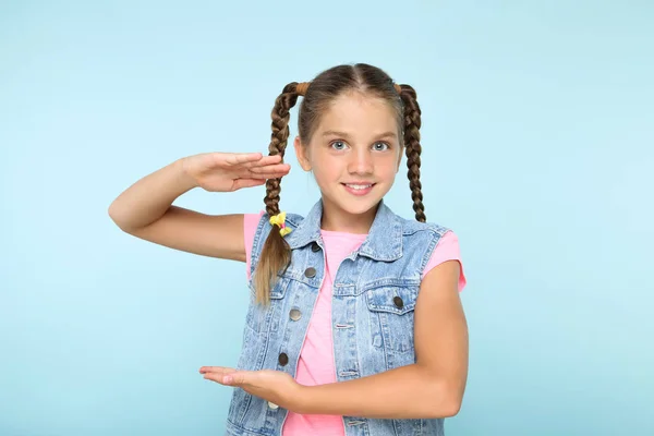 Menina bonita mostrando uma moldura por mãos no fundo azul — Fotografia de Stock