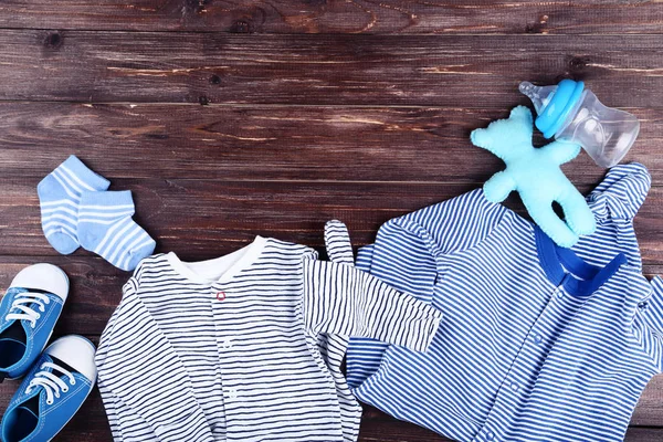 Baby clothes with soft bear toy and bottle on brown wooden table