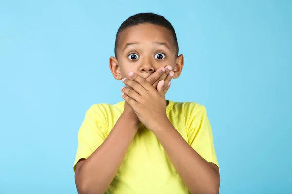 Милий американський хлопчик закриває рот руками на синьому фоні — стокове фото