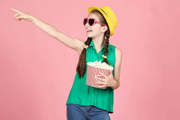 Krásná mladá dívka držící kbelík s popcornem na růžovém backgro — Stock fotografie
