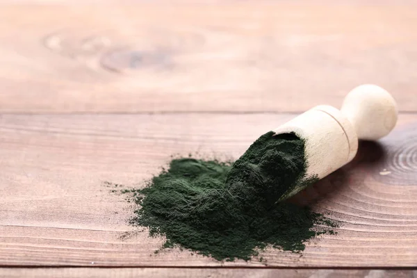 Spirulina powder with scoop on wooden table