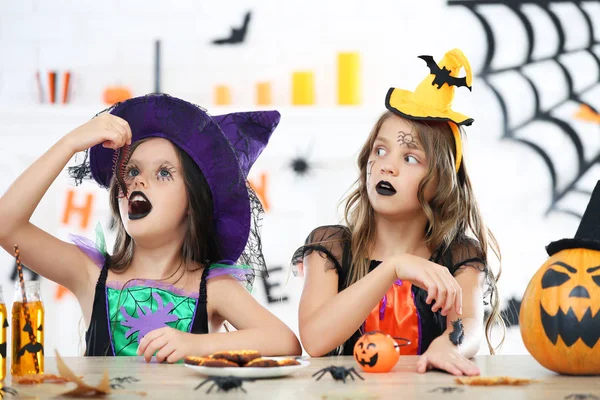 Beautiful two girls in halloween costumes sitting by the table a — Stock Photo, Image