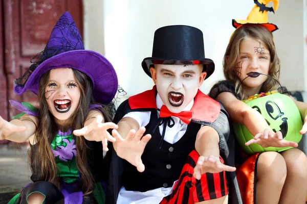 Due giovani ragazze e ragazzo in costumi di Halloween seduti sul portico — Foto Stock