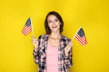 Sarı arka planda Amerikan bayrakları tutan genç kadın