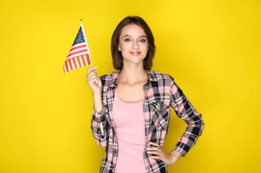 Sarı arka planda Amerikan bayrağı tutan genç kadın