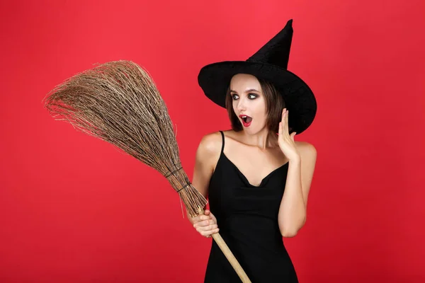 Šťastná mladá žena v černém Halloweenu, kostým s koštětem na červeném b — Stock fotografie