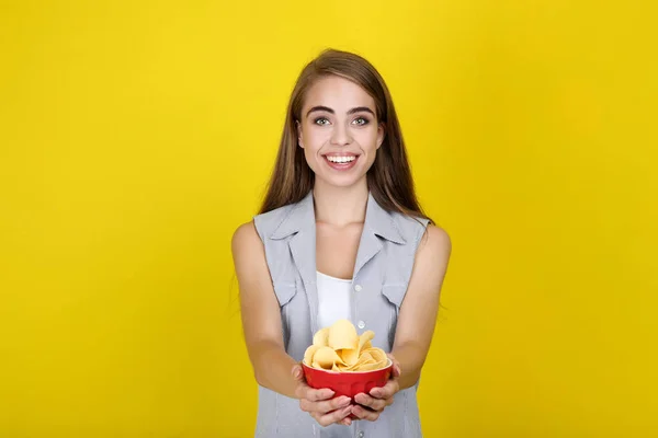 Młoda piękna dziewczyna z chipami ziemniaczanym w misce na żółtym backgro — Zdjęcie stockowe