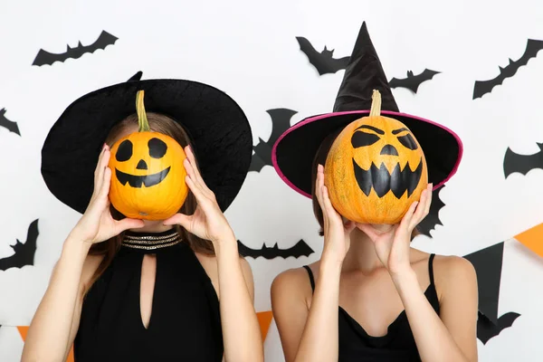 Duas jovens mulheres em trajes pretos segurando abóboras halloween sagacidade — Fotografia de Stock