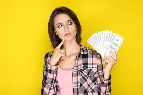 Ung kvinna som innehar dollarsedlar på gul bakgrund — Stockfoto