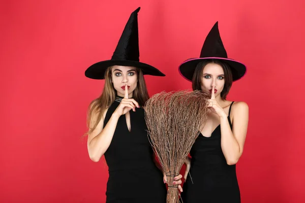 Duas jovens mulheres em trajes de Halloween preto com vassoura em vermelho ba — Fotografia de Stock