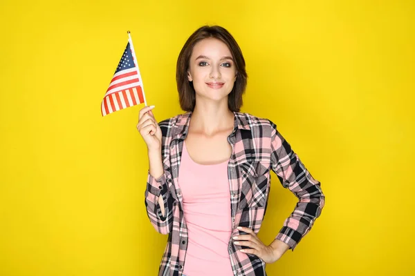 Young woman holding american flag on yellow background — Stock Photo, Image