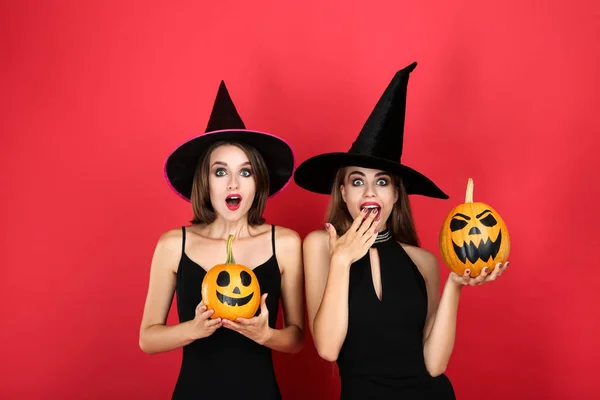 Duas jovens mulheres em trajes pretos com abóbora halloween no vermelho — Fotografia de Stock