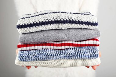 Gri arka planda katlanmış örgü süveter tutan kadın elleri
