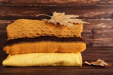 Kahverengi ahşap masada sonbahar yapraklı katlanmış süveterler.