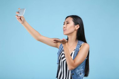 Mavi arka planda akıllı telefondan selfie çeken genç bir kadın.