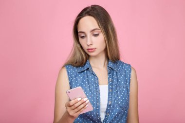 Pembe arka planda cep telefonu olan güzel bir kadın.
